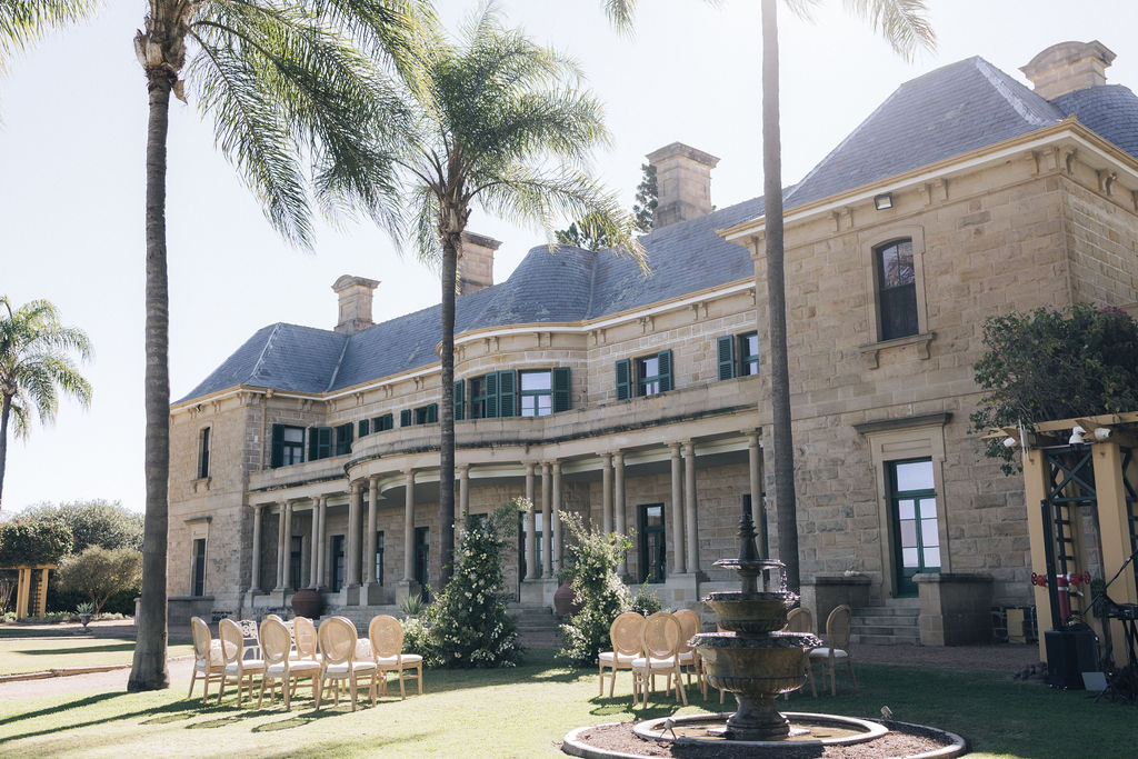 Outdoor wedding setup on the lawn at Jimbour House, featuring classic French-style chairs and a central water fountain in front of the heritage sandstone homestead.