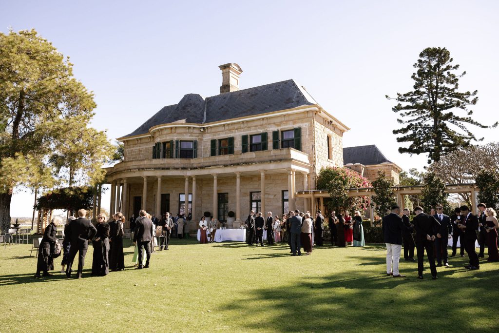 Guests gather on the Eastern Lawn at Jimbour House for a garden cocktail hour, with the sandstone homestead and verandah in the background at a Queensland wedding venue