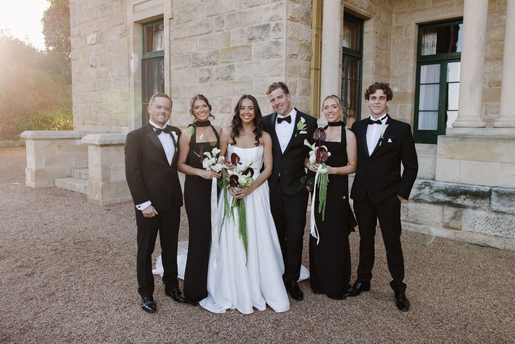 Bridal party portrait in front of Jimbour House with bride and groom and attendants in formal black attire Queensland wedding venue