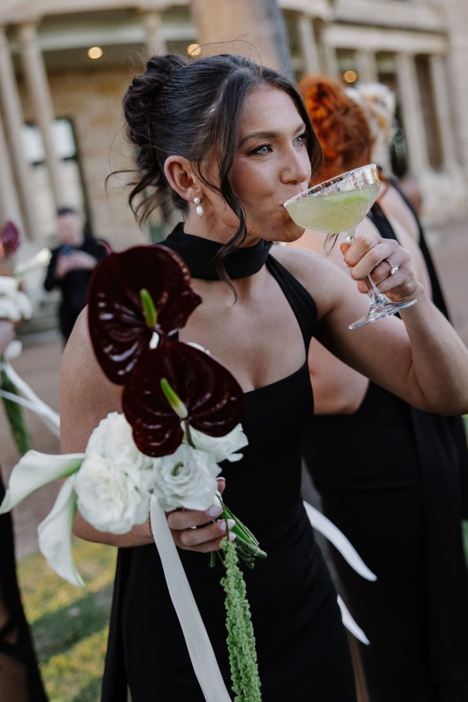 Wedding guest holding calla lilies and anthurium bouquet while sipping a cocktail during outdoor cocktail hour at Jimbour House Queensland
