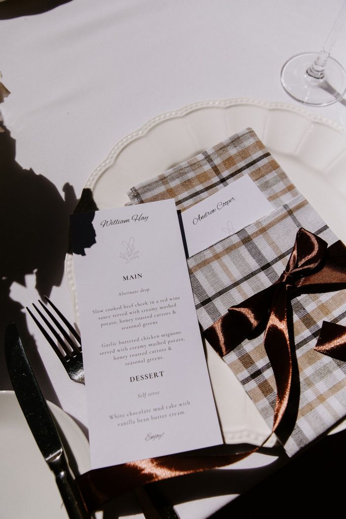 Elegant wedding place setting at Jimbour House in Queensland featuring custom menu card, name card, checkered napkin, and satin ribbon styling for a destination wedding reception.