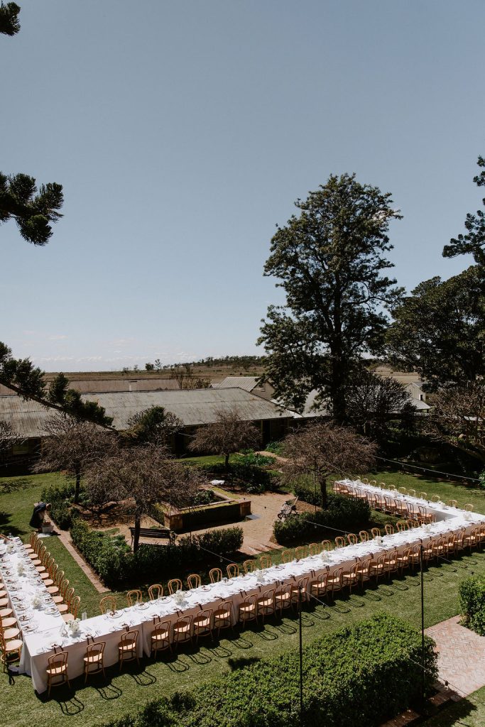 Elegant outdoor wedding reception setup in the courtyard at Jimbour House in Queensland, with long banquet tables arranged in a U-shape for a destination wedding celebration.