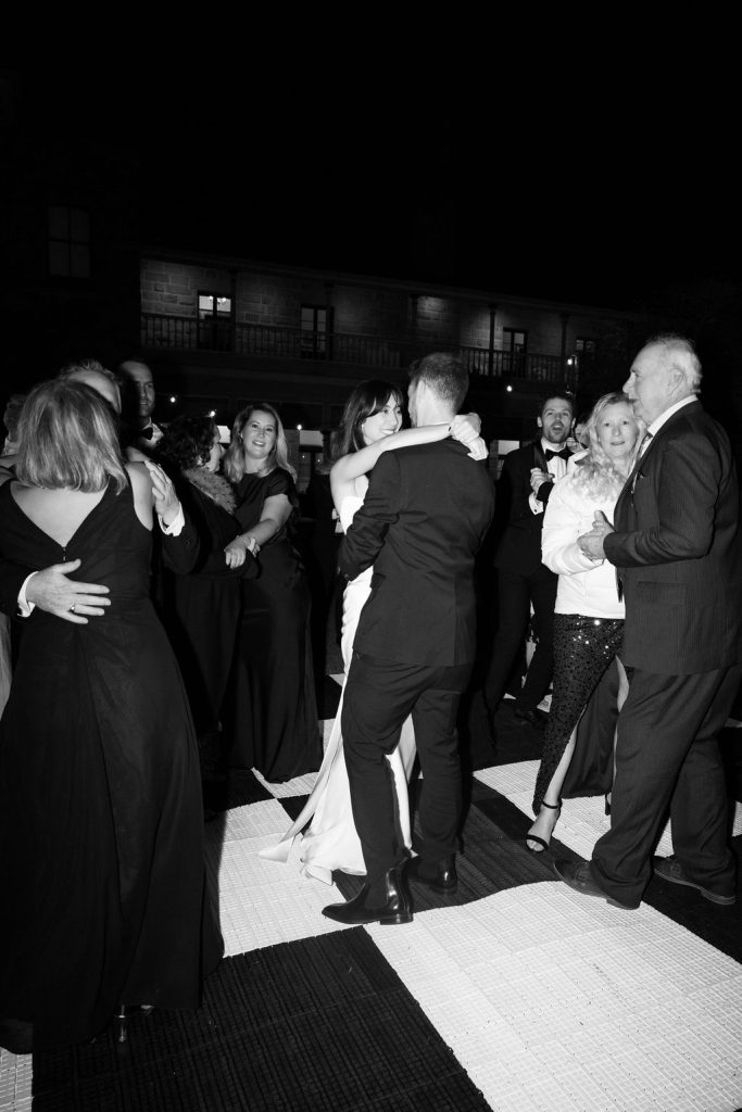 Bride and groom kissing on the lawn at Jimbour House with bridal party holding parasols, sandstone homestead in the background at a Queensland wedding venue