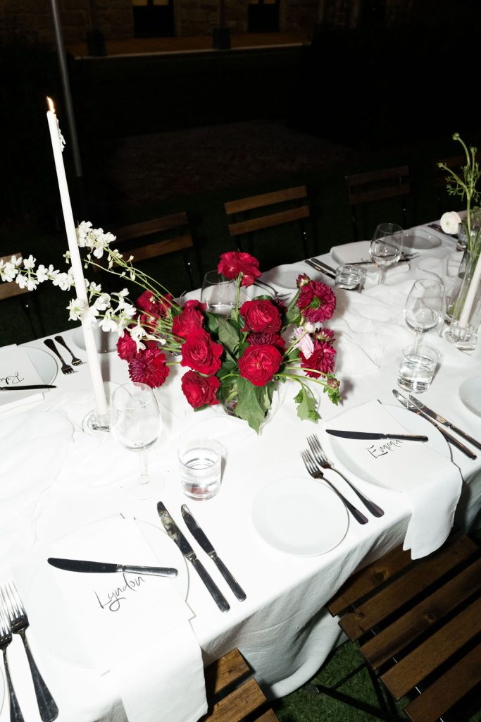 Outdoor wedding reception table at Jimbour House with white linen, red rose floral centrepiece and candlelight styling set for evening dining in the courtyard
