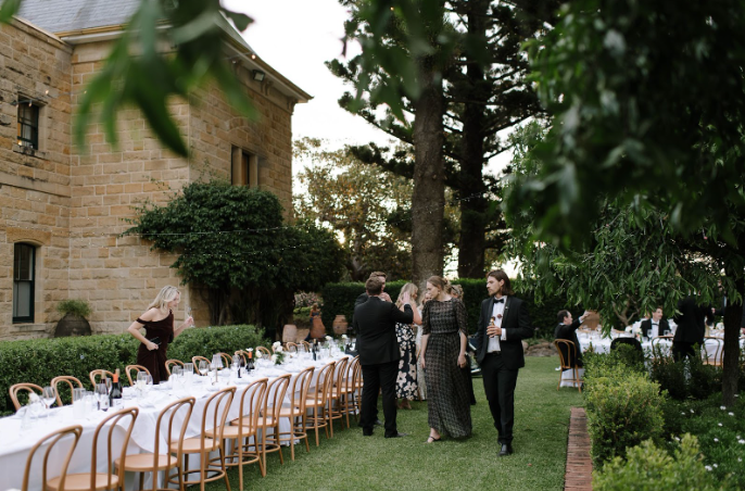 Guests mingling beside long banquet tables during an outdoor garden wedding reception at Jimbour House with sandstone buildings and greenery surrounding the courtyard
